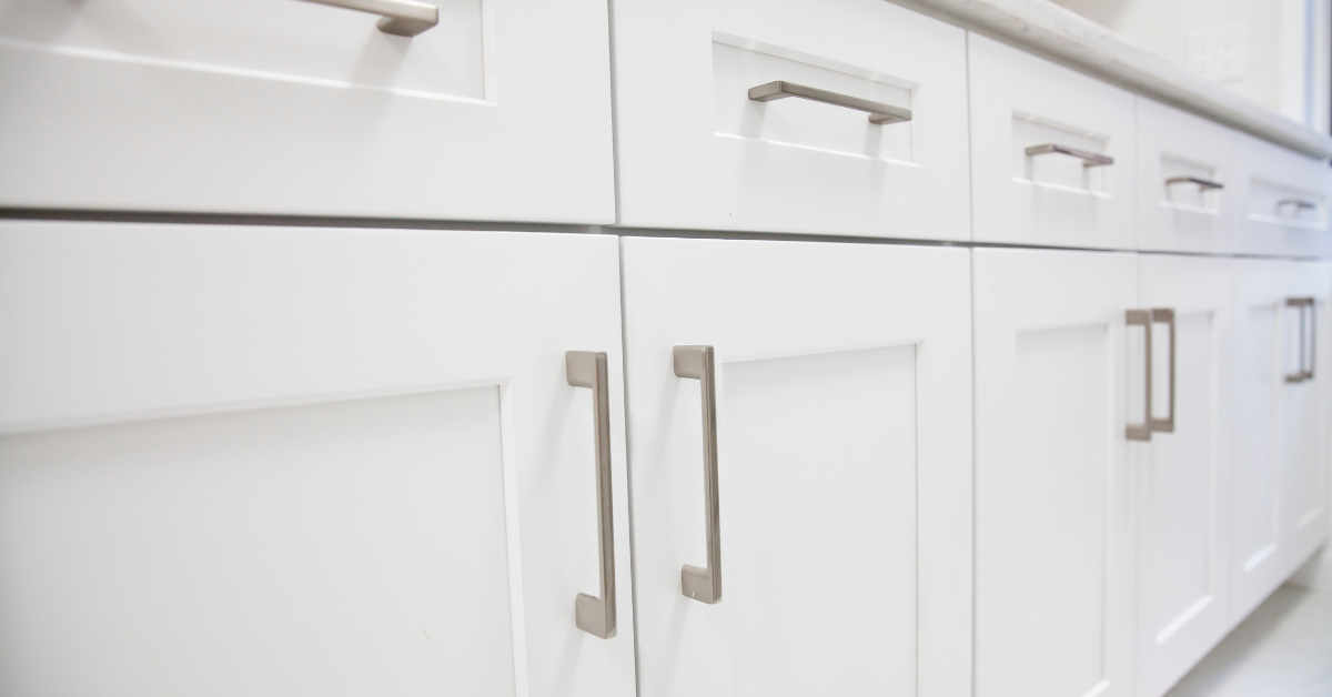 Close-up of freshly painted white kitchen cabinet doors with modern brushed metal handles and clean panel design.